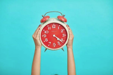 person holding red and beige twin bell analog alarm clock