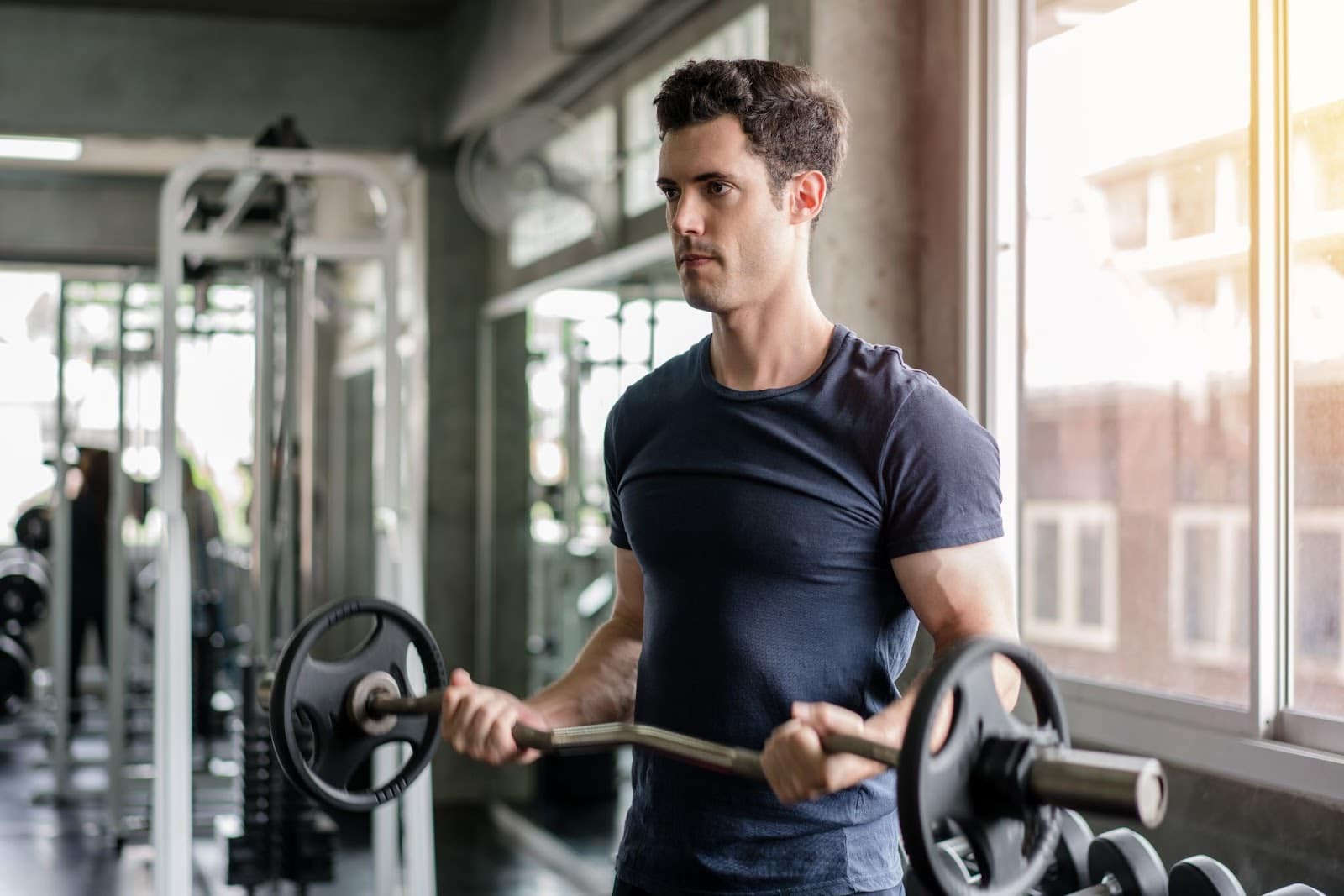 Fit young man wearing a blue shirt performing a bicep curl with a barbell. 