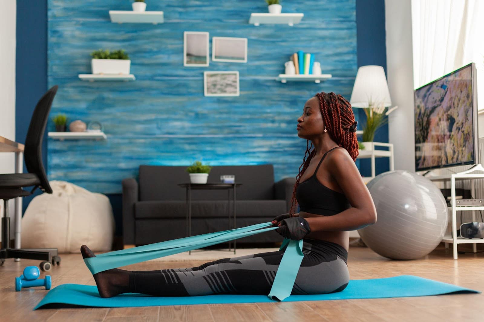 Young black, fit woman on the ground performing a seated row with a resistance band.