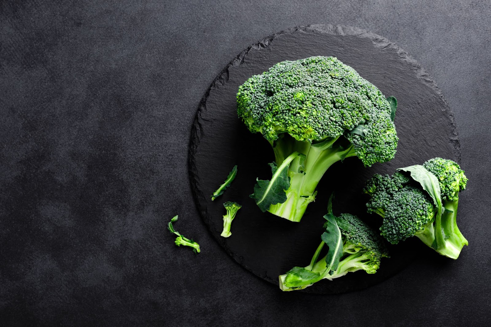 Image of bunches of broccoli over a black slate plate.