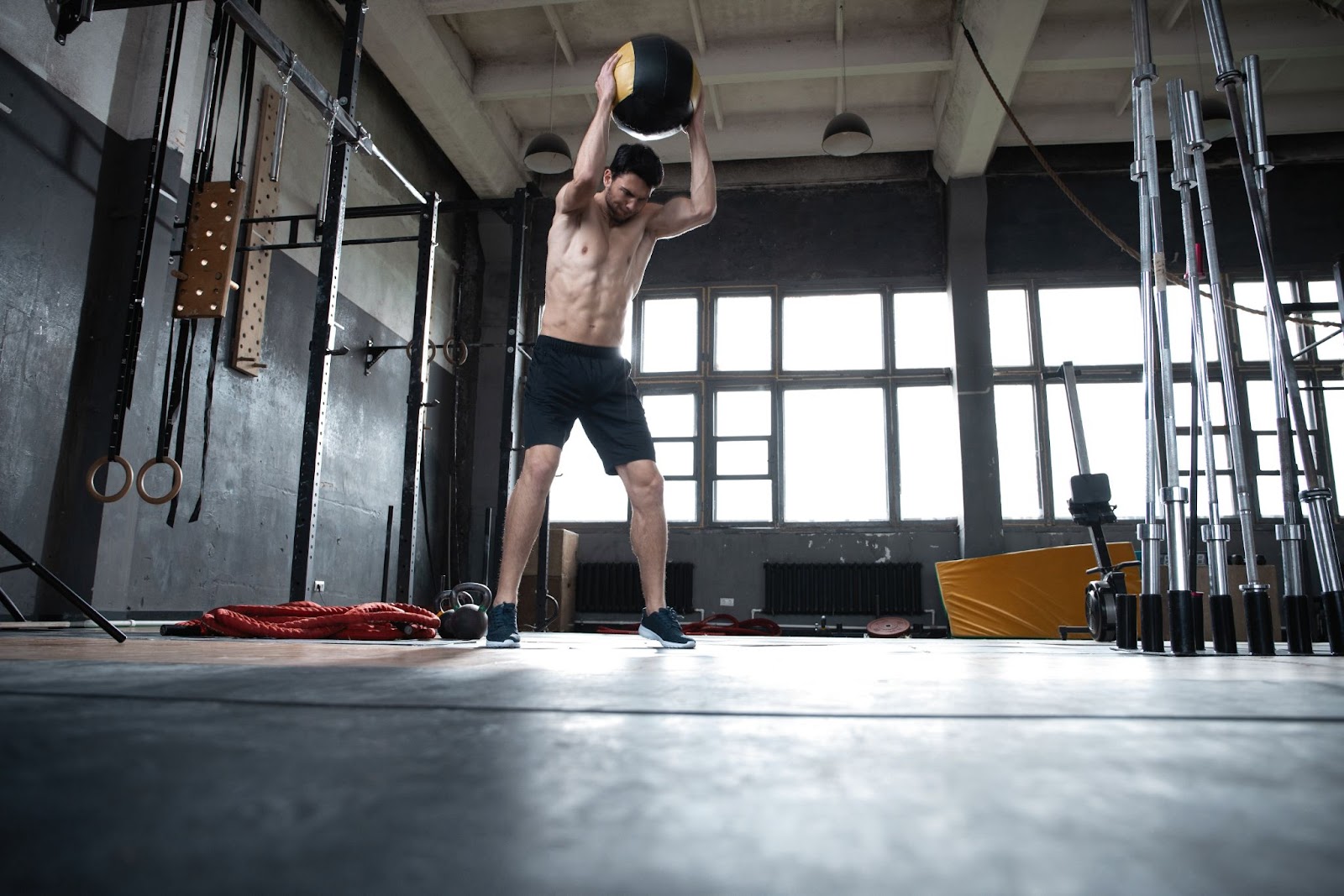 Man without a shirt on performing a medicine ball slam in an empty gym.