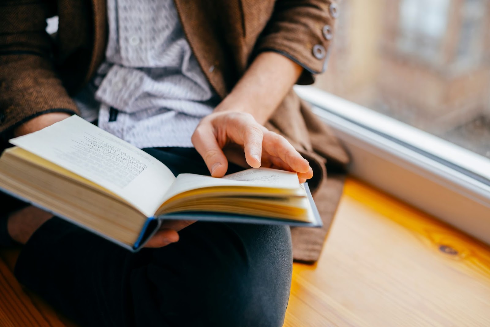 Person sitting on a window sill reading a book