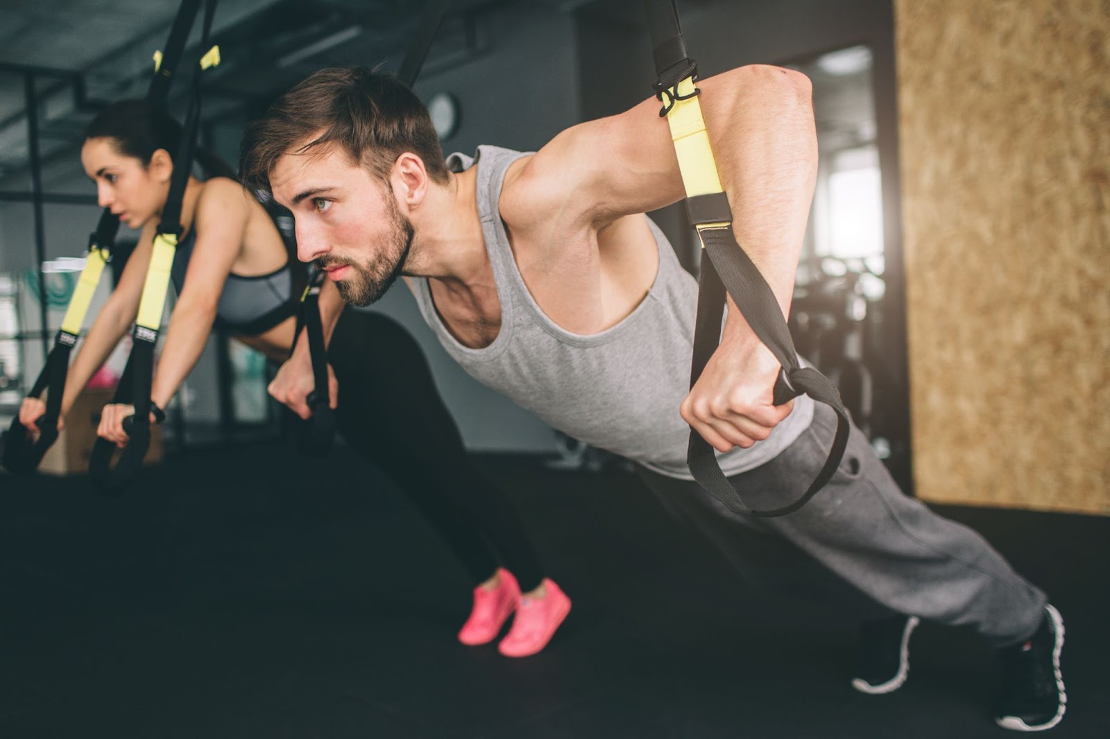 Young fit man and woman doing a chest press with TRX straps