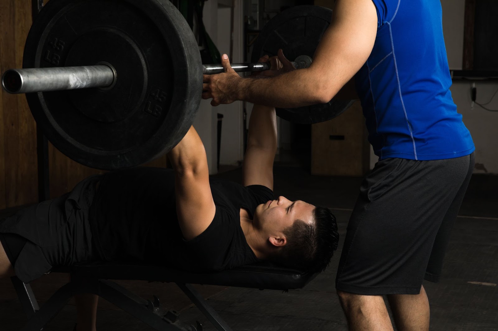 Man spotting another man at a gym, doing a bench press