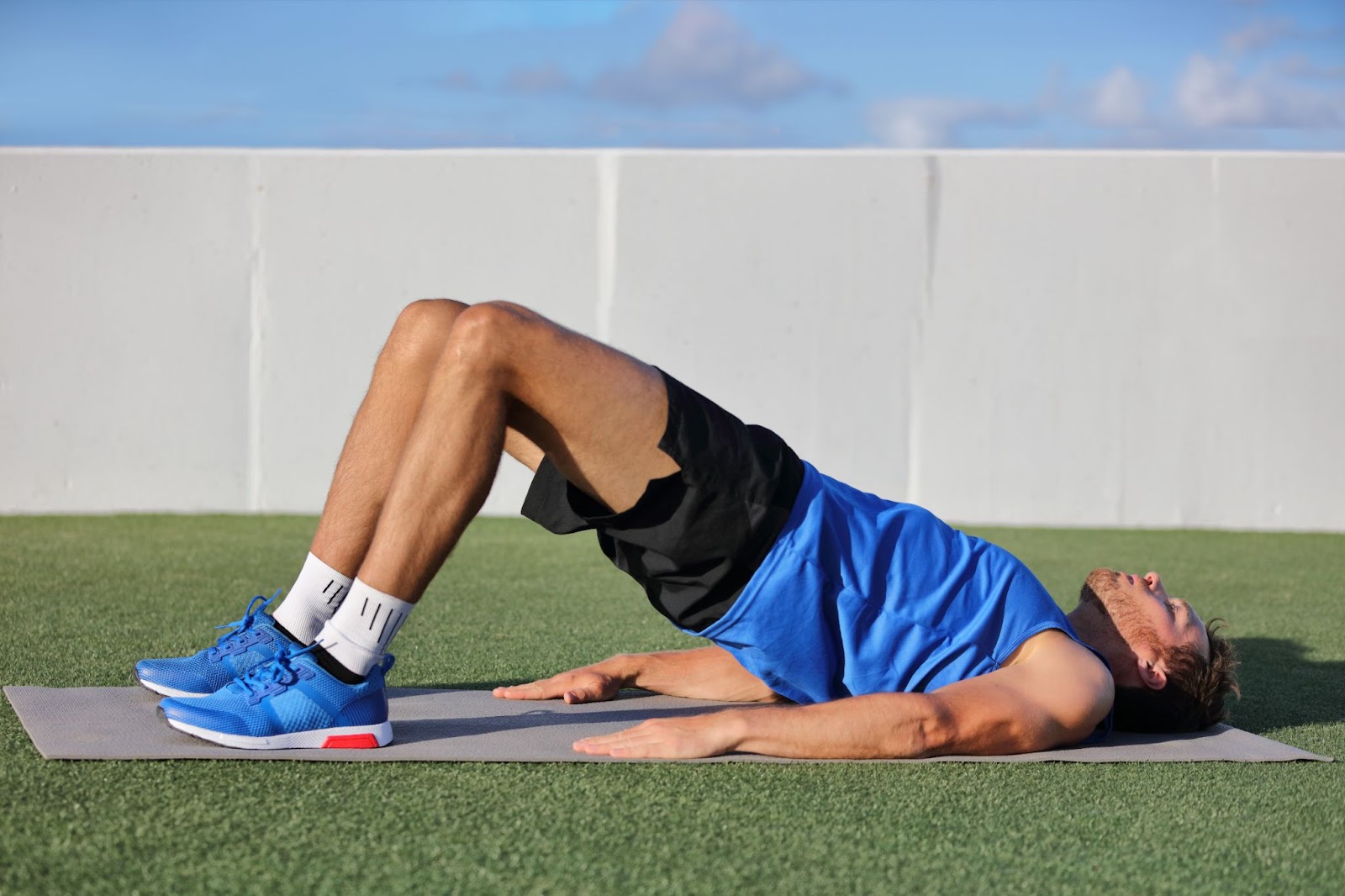 Man in a field doing a glute bridge on astro turf