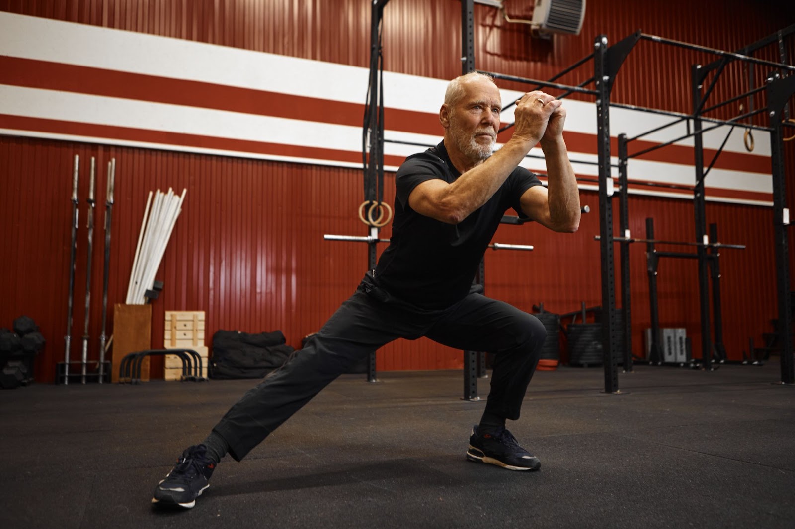 Older gentleman dressed in black athletic wear doing a side lunge in a gym