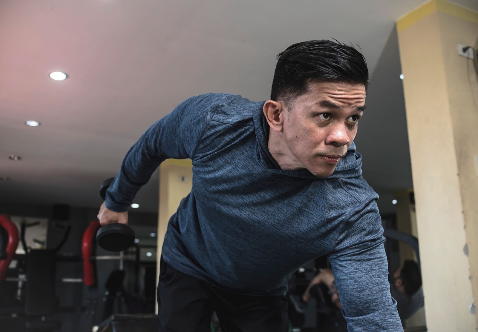 Young man in a blue long-sleeved shirt performing a dumbbell kickback