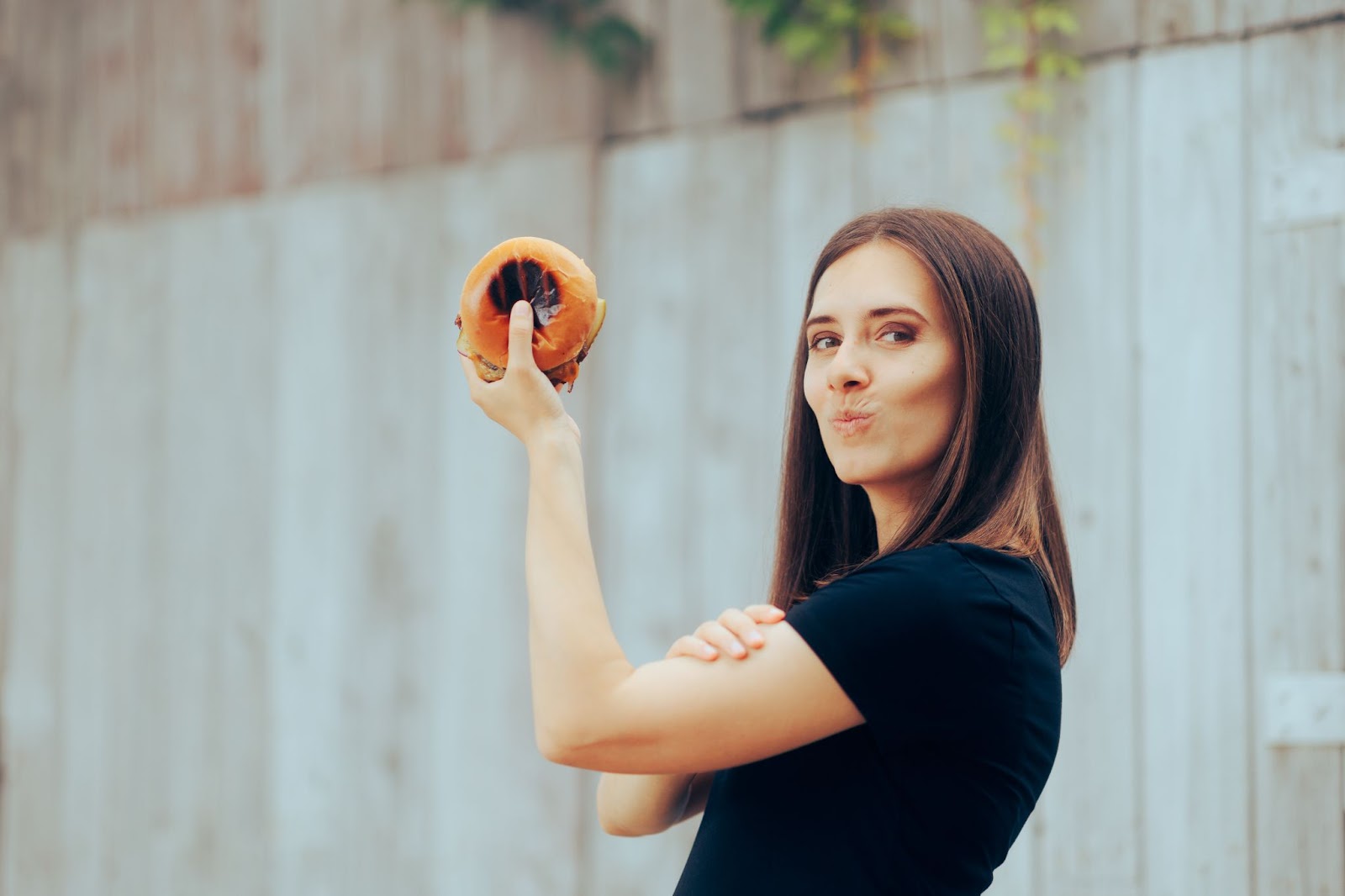 Young woman holding a hamburger and feeling strong and powerful