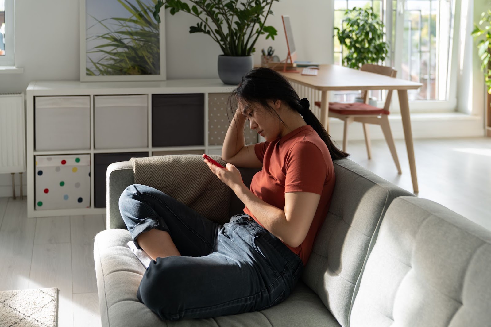 Young woman lazily scrolling on phone while laying on a couch