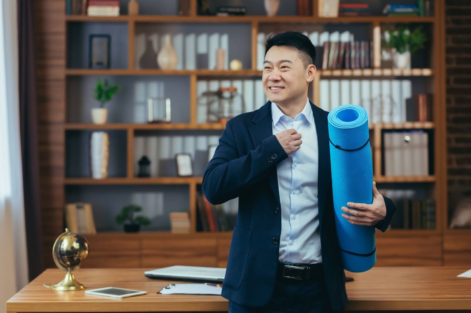 Fit businessman holding a yoga mat in his office