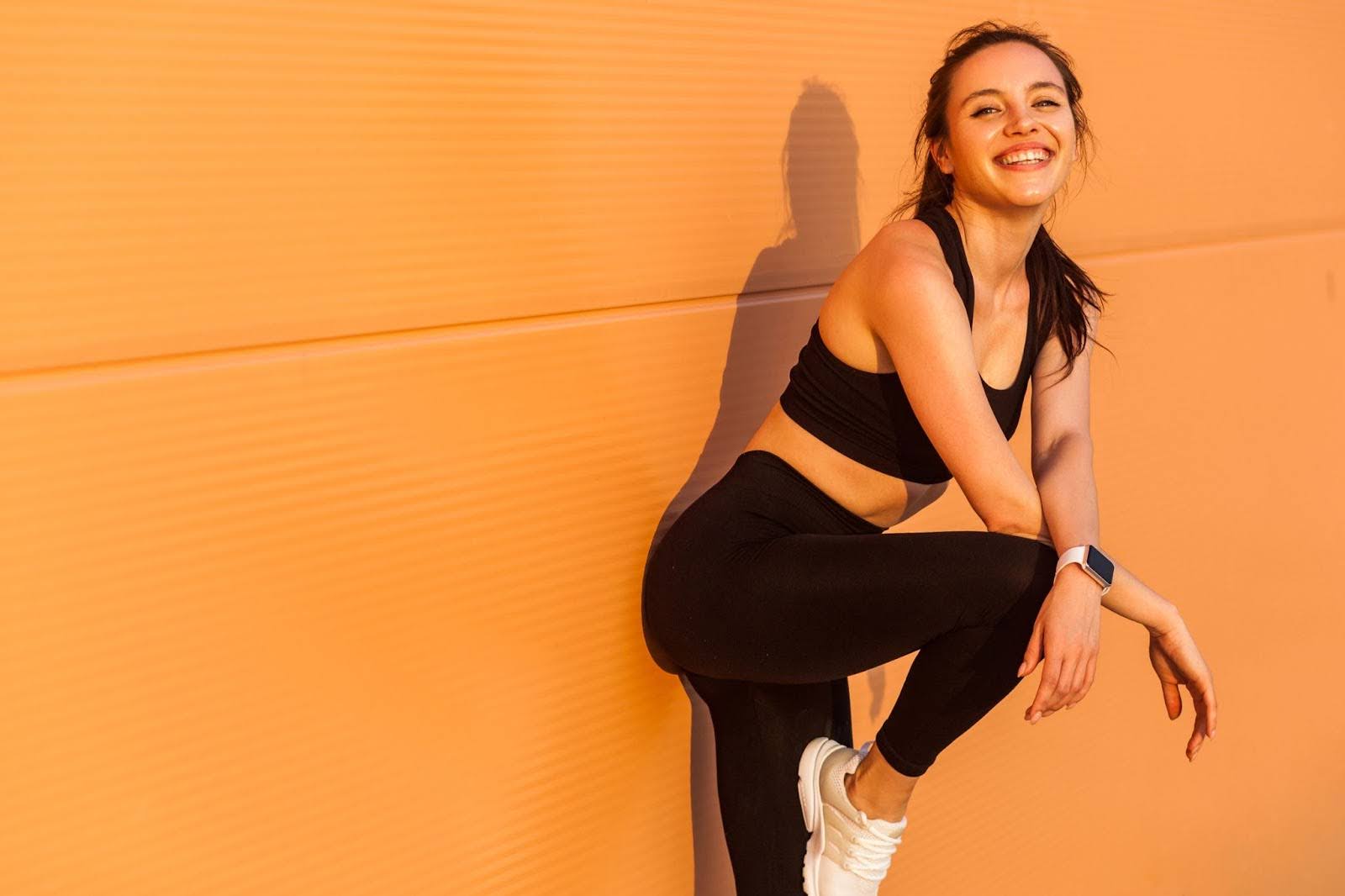 Fit woman leaning up against an orange wall after a Pilates workout