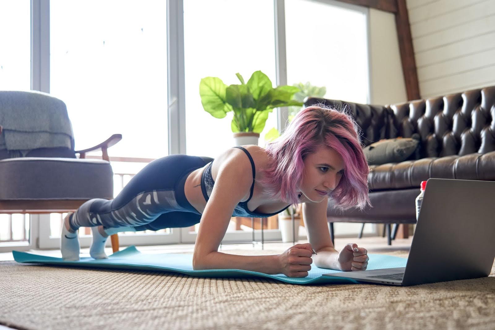 Woman with pink hair taking a fitness class from the comfort of her home