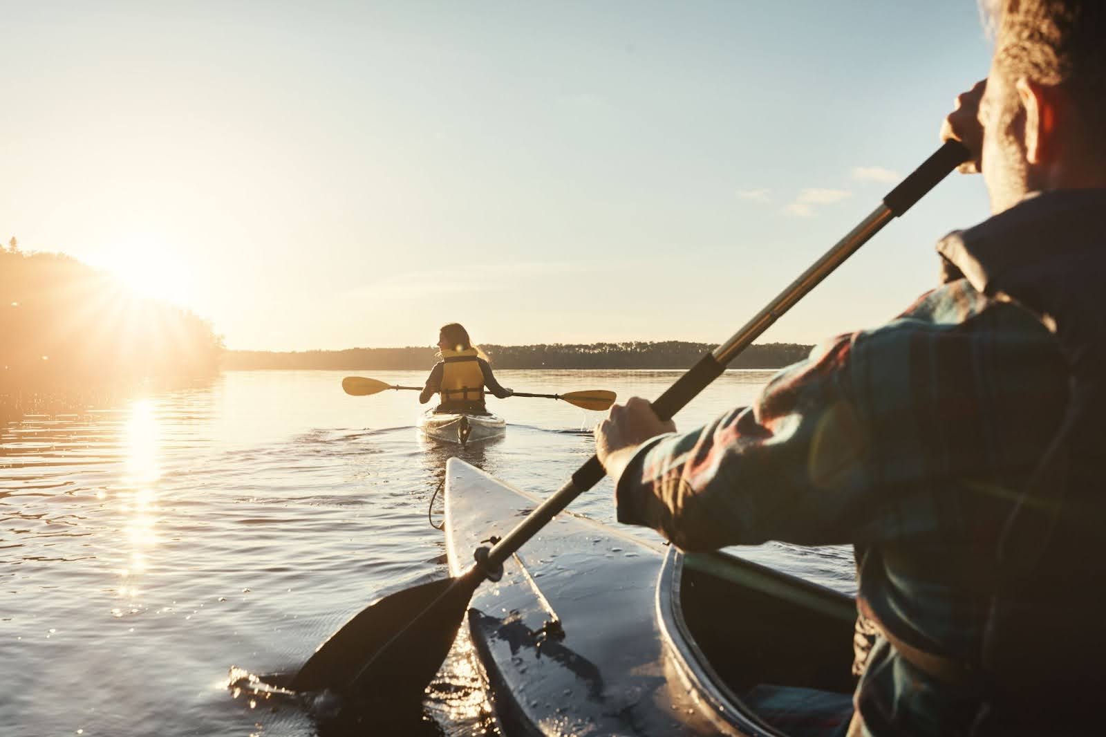 Couple rowing on two kayaks in a large lake at sunset