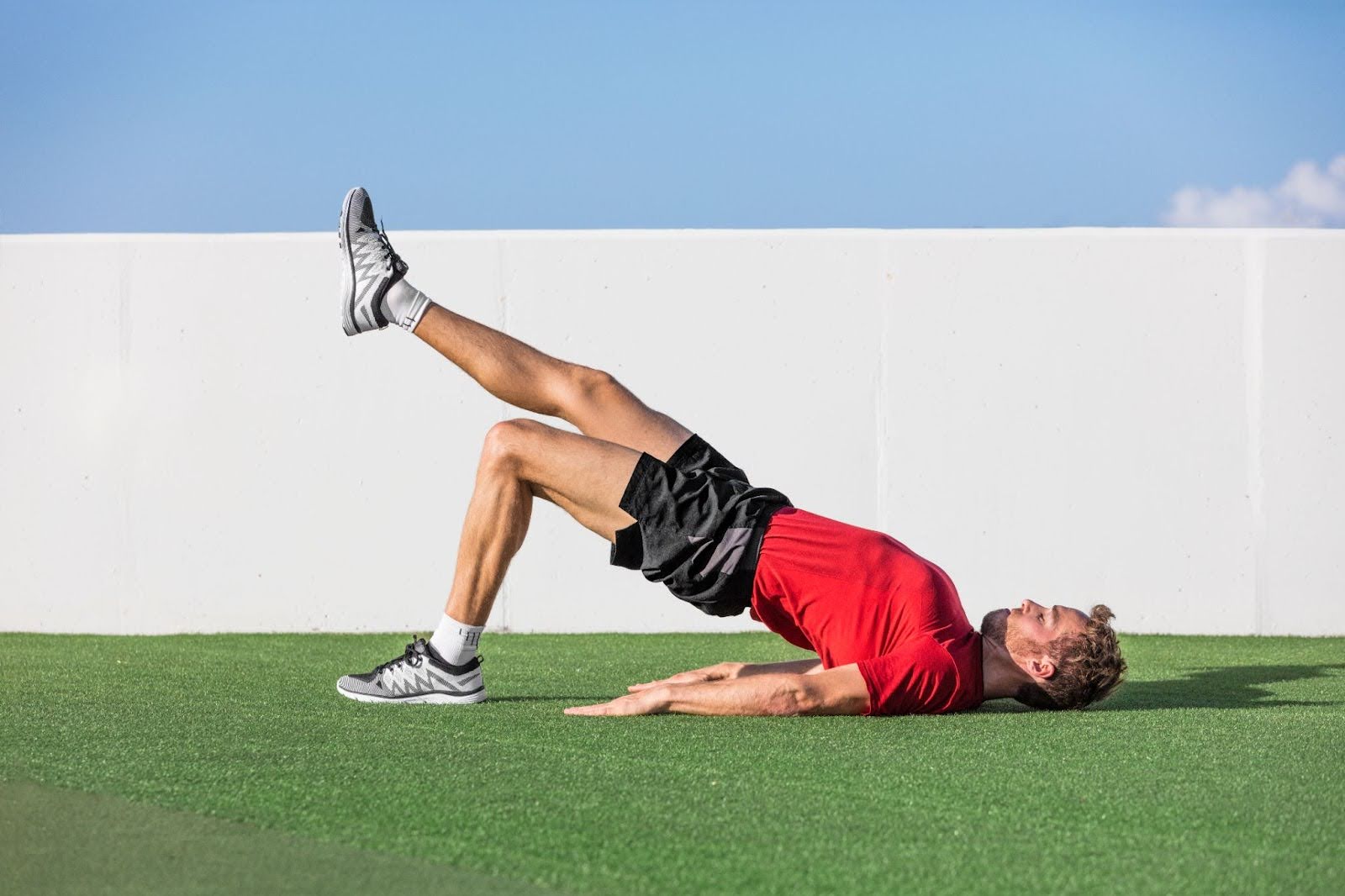 Man performing a glute bridge with raised arms inside a fitness studio